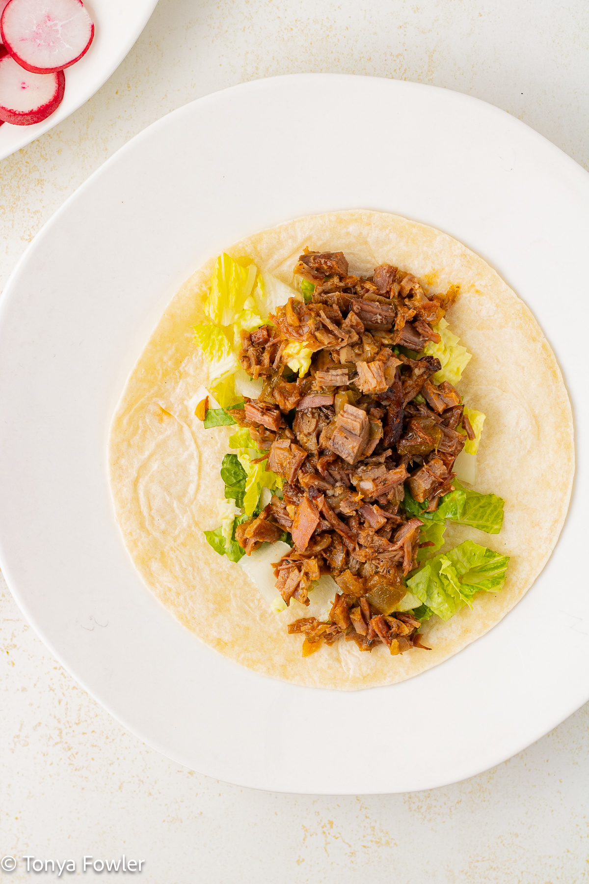 Overhead view of a tortilla topped with beef and lettuce.