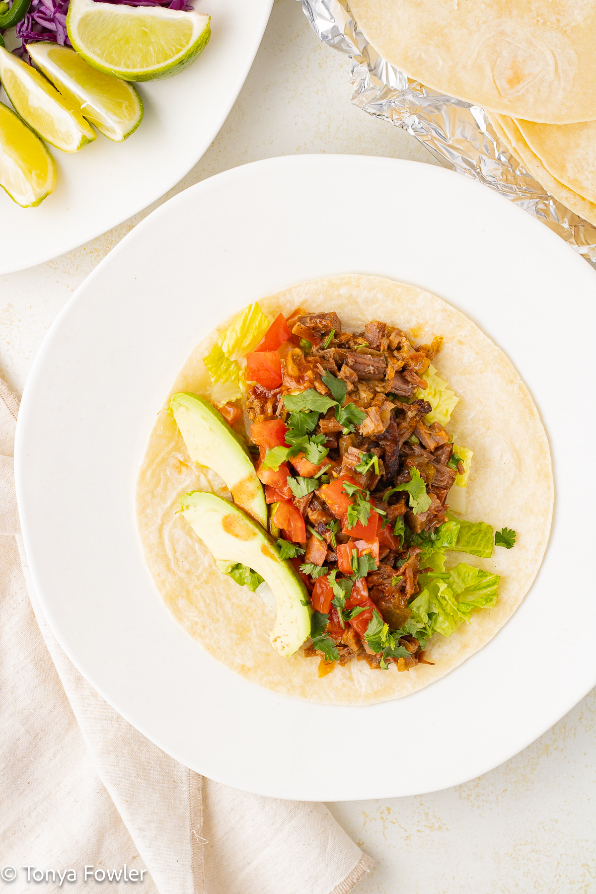 Overhead view of a tortilla topped with beef, lettuce, tomatoes and sliced avocados.