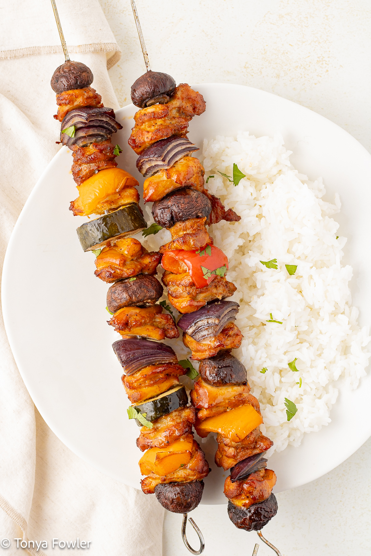 Overhead view of cooked chicken kabobs on a plate with rice.
