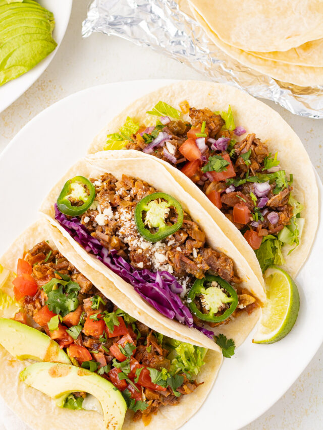 Overhead view of tacos on a plate with lime wedges.