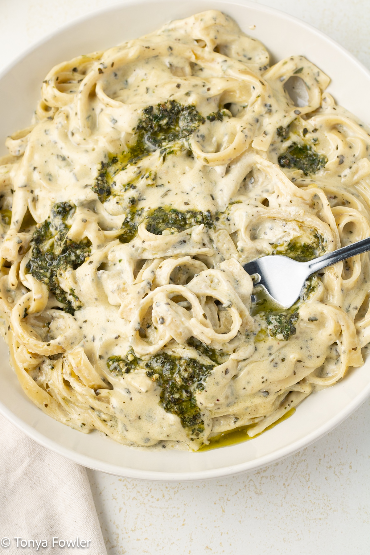 Close up image of a bowl of alfredo pasta with a bowl topped with pesto sauce.