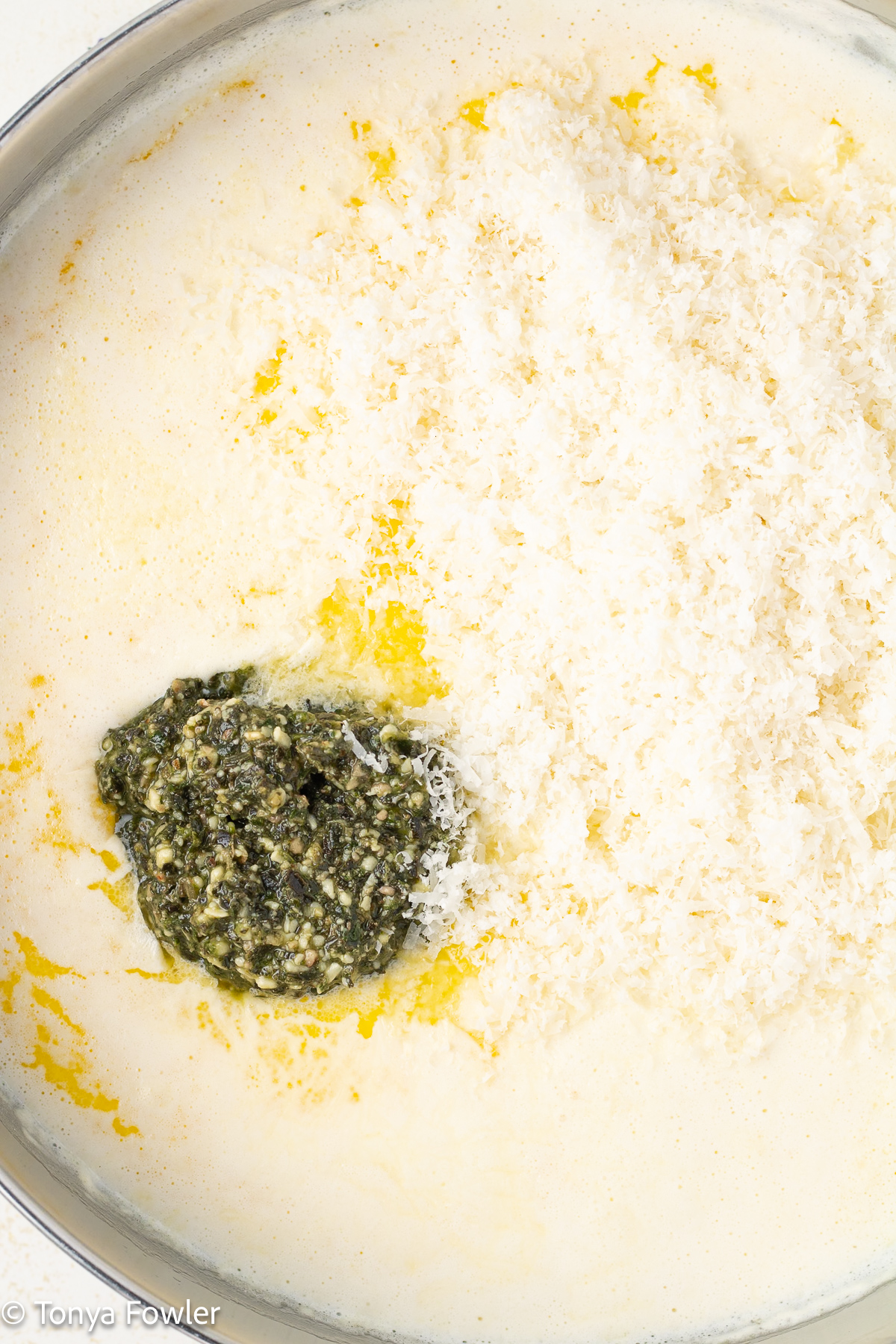 Cream sauce in a skillet topped with basil pesto and grated cheese.