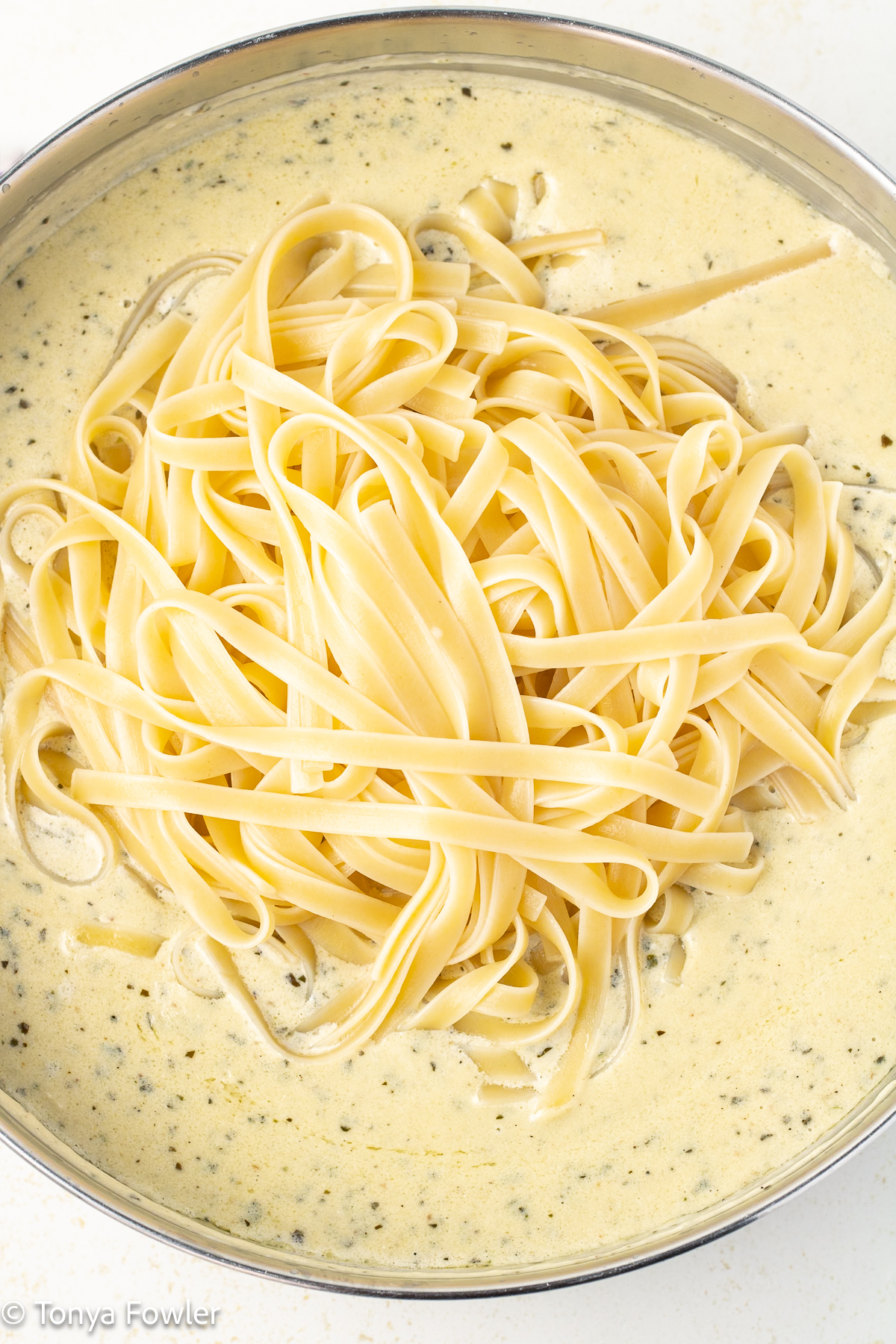 White sauce in a skillet with cooked pasta.