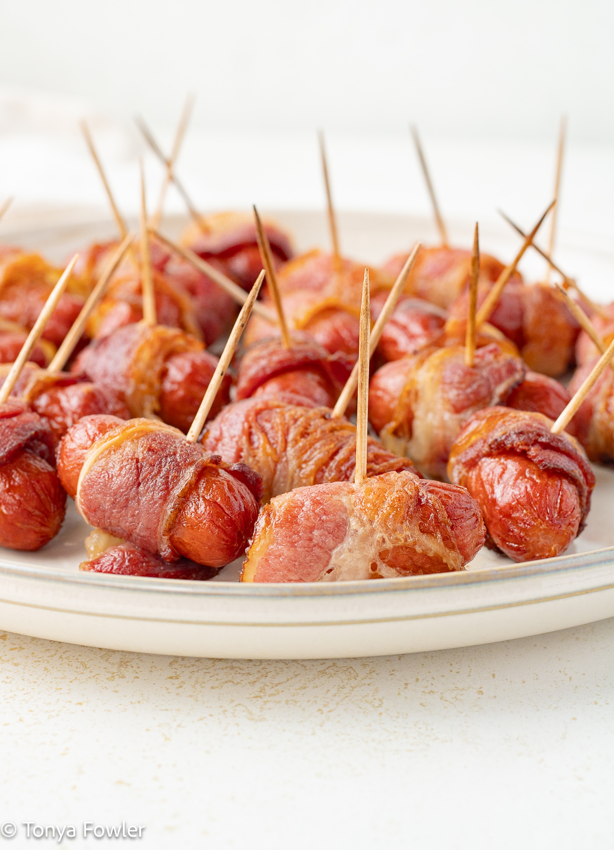 Straight on view of bacon wrapped hot dogs on a plate with toothpicks.