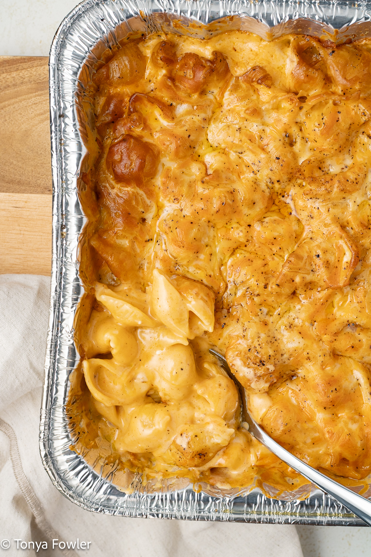 Pan of smoked mac and cheese sitting on a cutting board with a spoon.