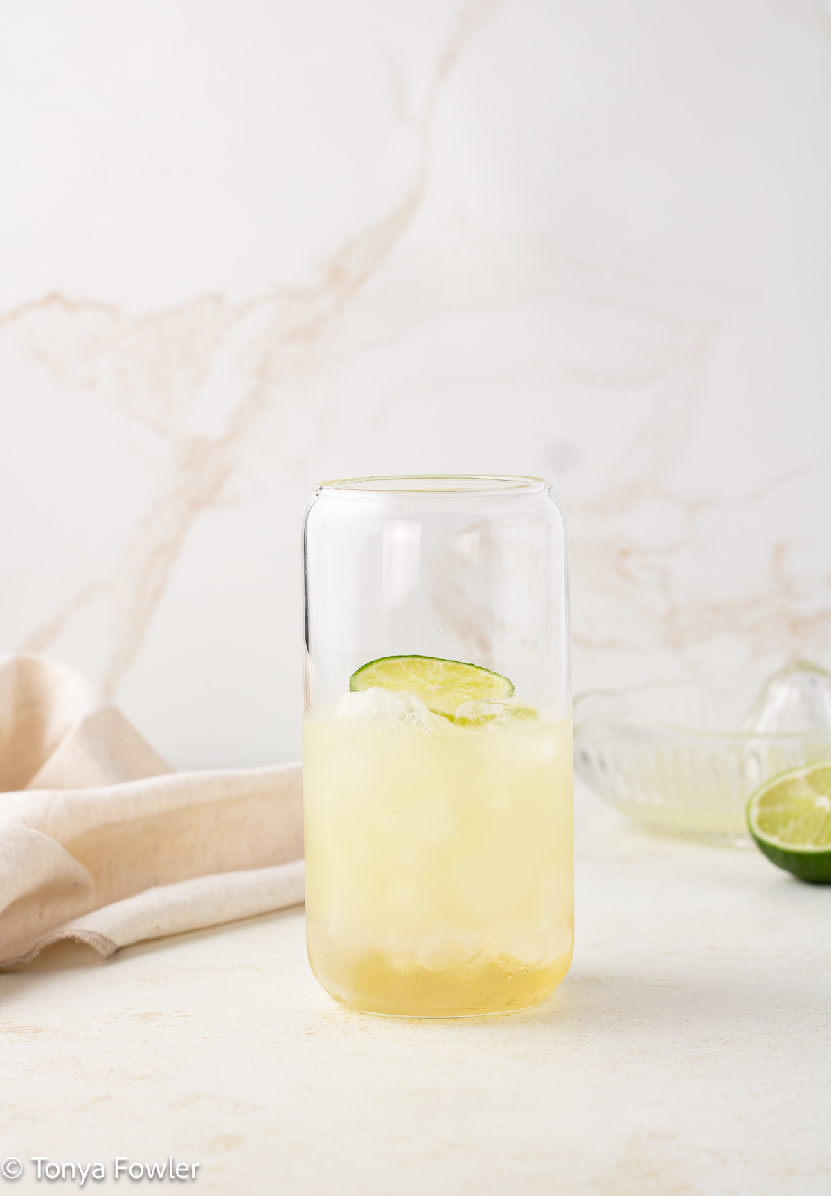 Straight on view of a glass filled with ice, lime juice and a slice of lime.