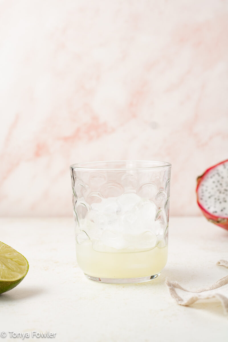 Straight view of a glass filled with ice and lime juice.