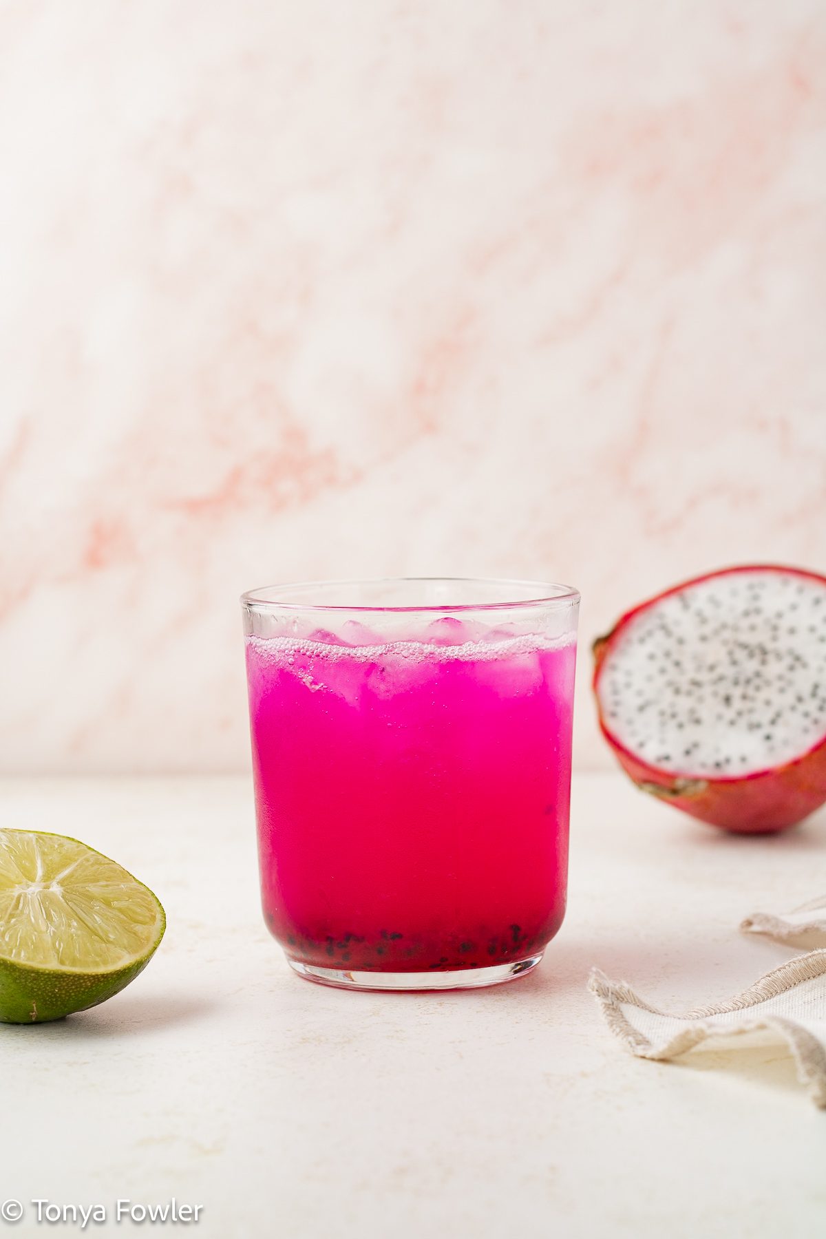 Straight on view of dragon fruit mocktail with fresh dragon fruit and lime on the counter.