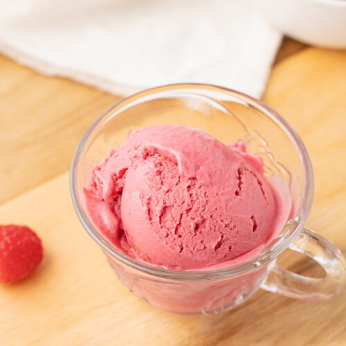 A scoop of frozen yogurt in a cup with fresh raspberries all around.