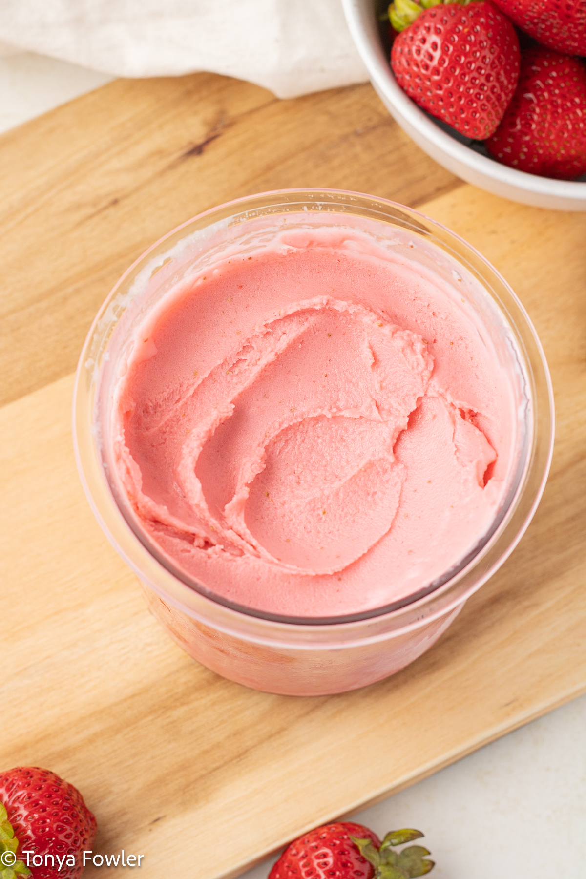 Ninja Creami strawberry Frozen Yogurt in a pint container with fresh strawberries near by.