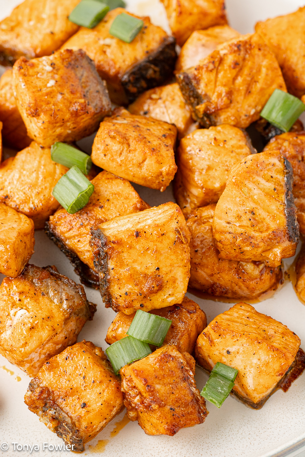 Salmon nuggets on a plate with sliced green onions.