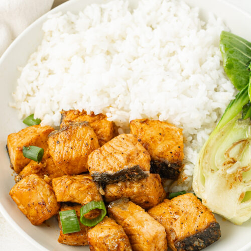 3/4 view of salmon bites on a plate with rice and bok choy.