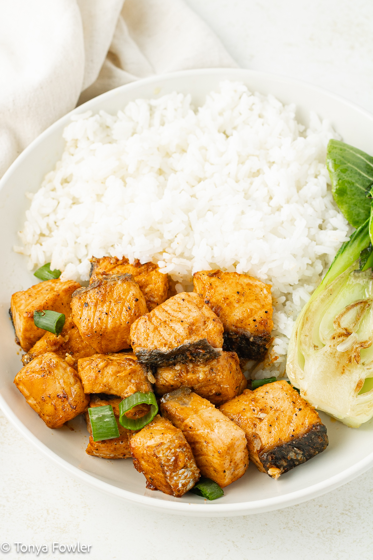 3/4 view of salmon bites on a plate with rice and bok choy.