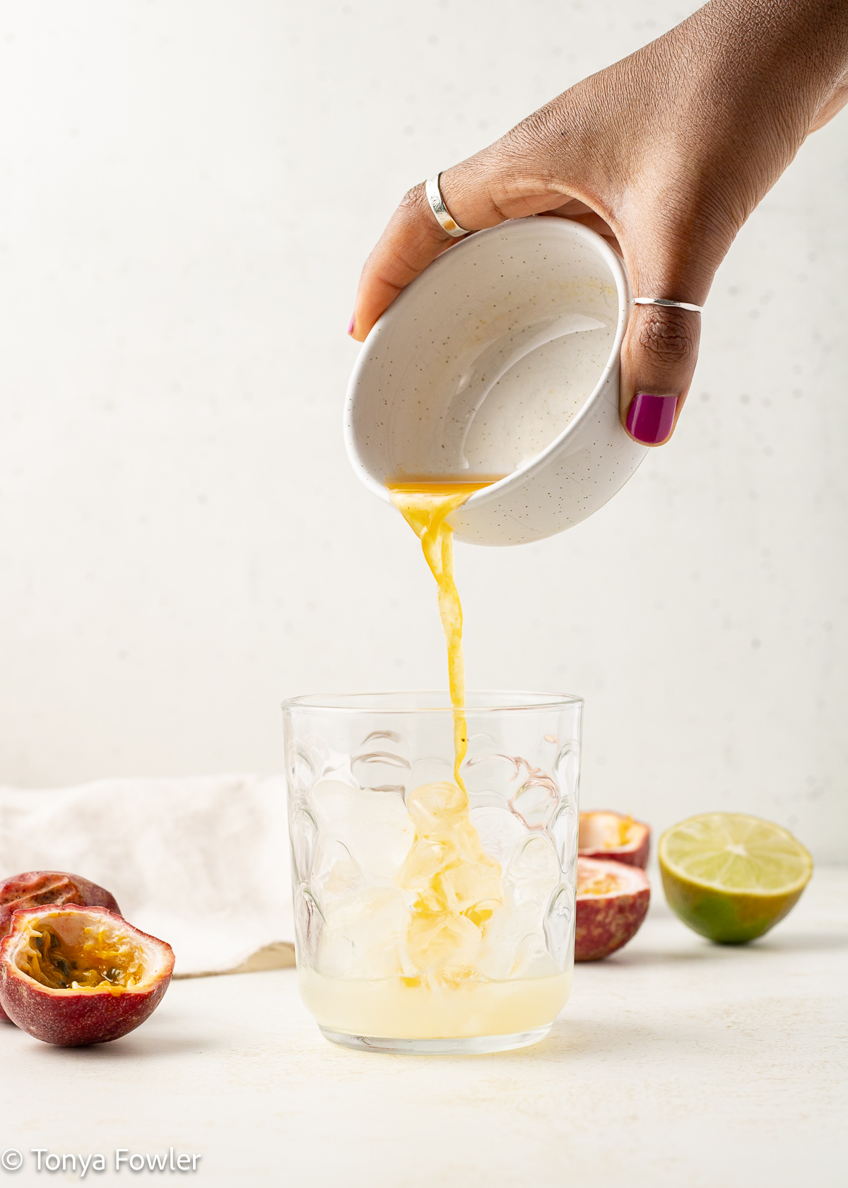 A woman's hand pouring syrup in a glass with ice.