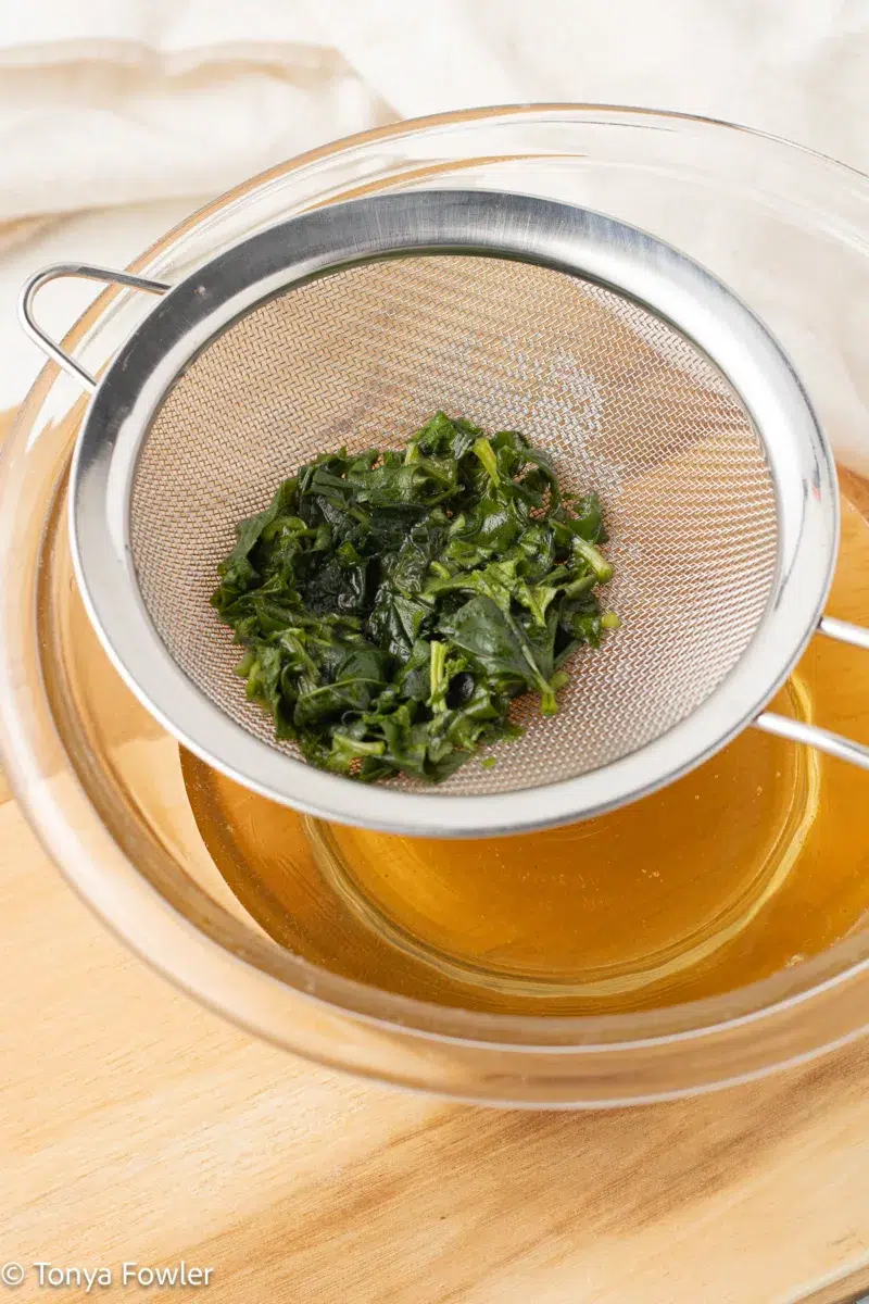 Cooked basil being strained out of the syrup in the bowl.