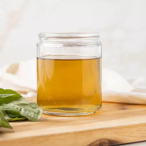 Basil syrup in a jar with fresh basil near by.