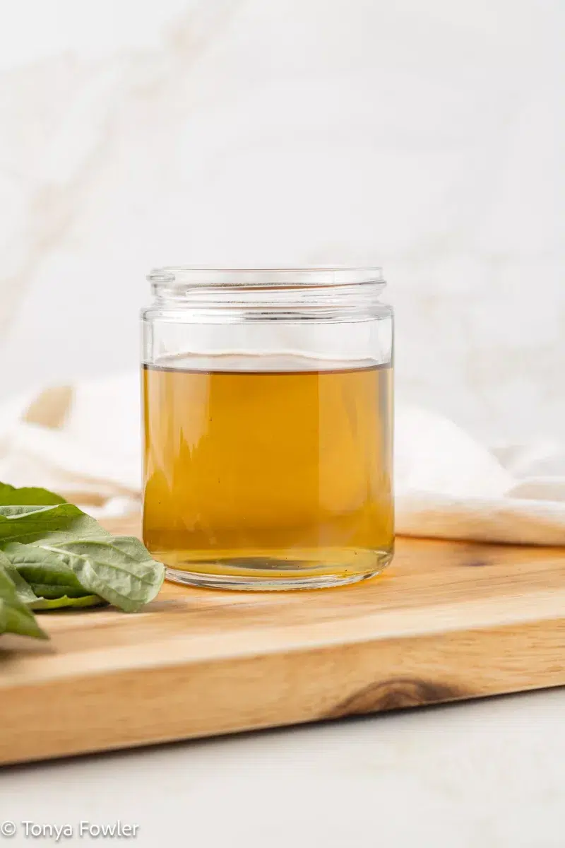 Basil syrup in a jar with fresh basil near by.