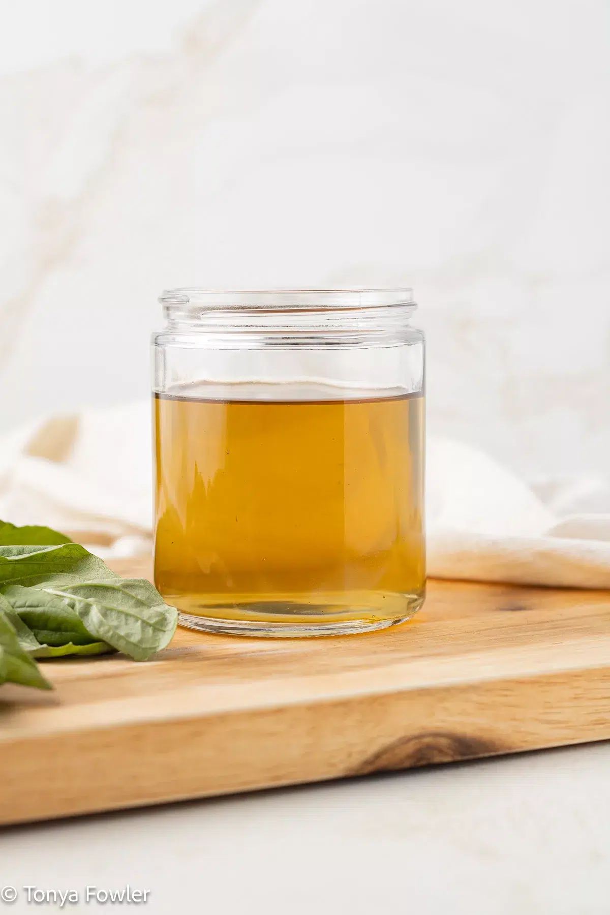 Basil syrup in a jar with fresh basil near by.