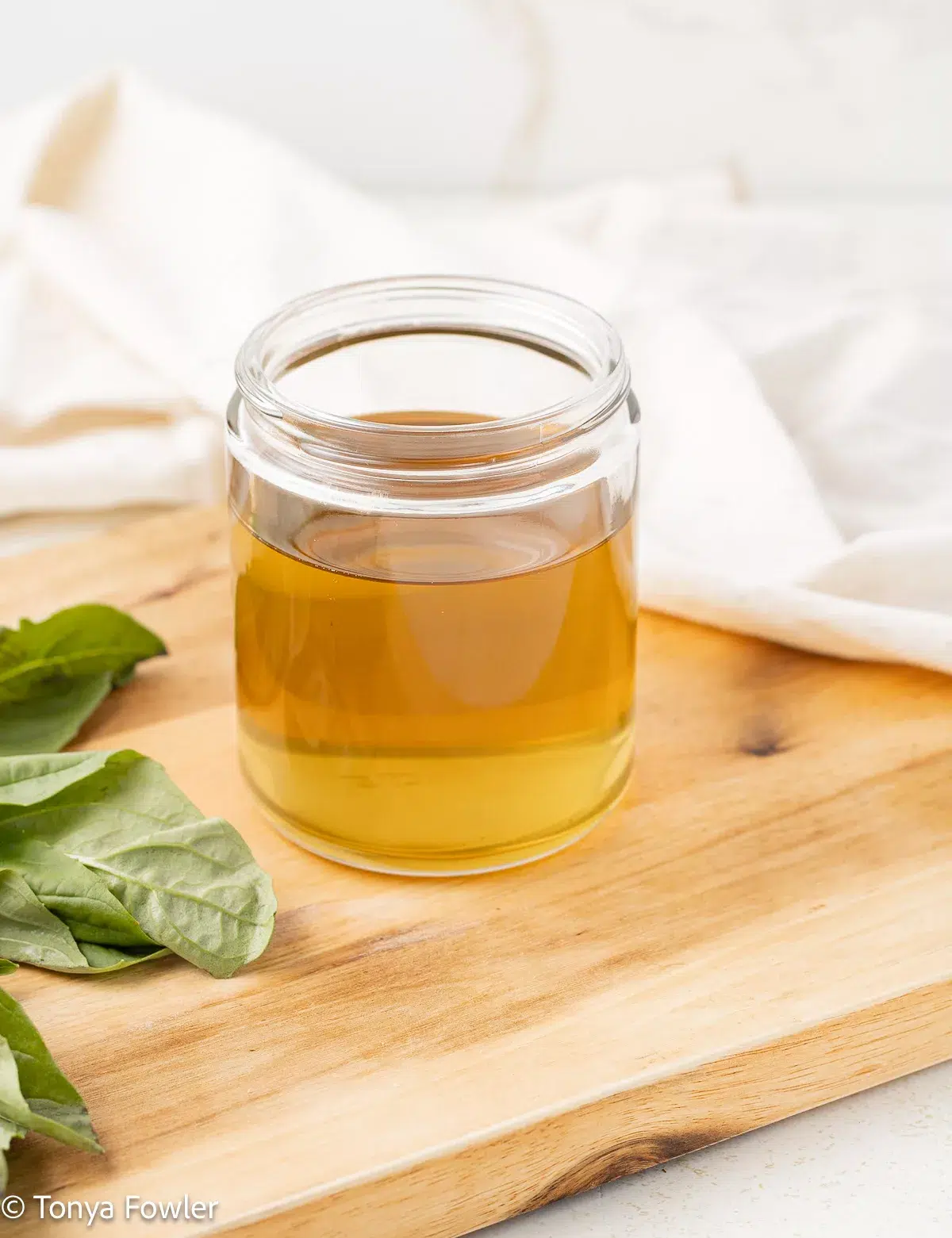 3/4 view of syrup in a jar sitting on a cutting board with fresh herbs near by.
