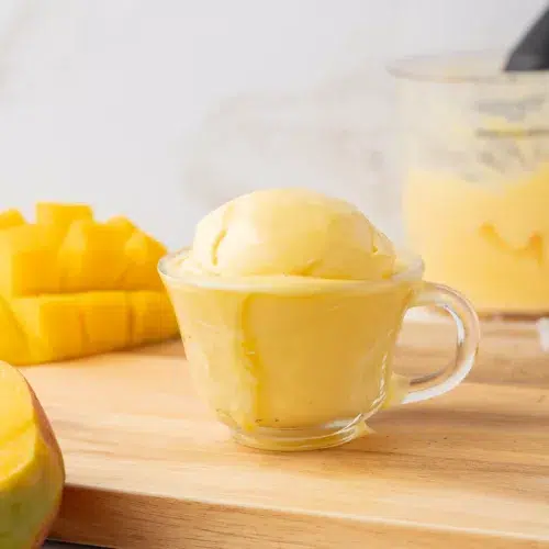 Straight on view of mango frozen yogurt in a cup with fresh mango near by.
