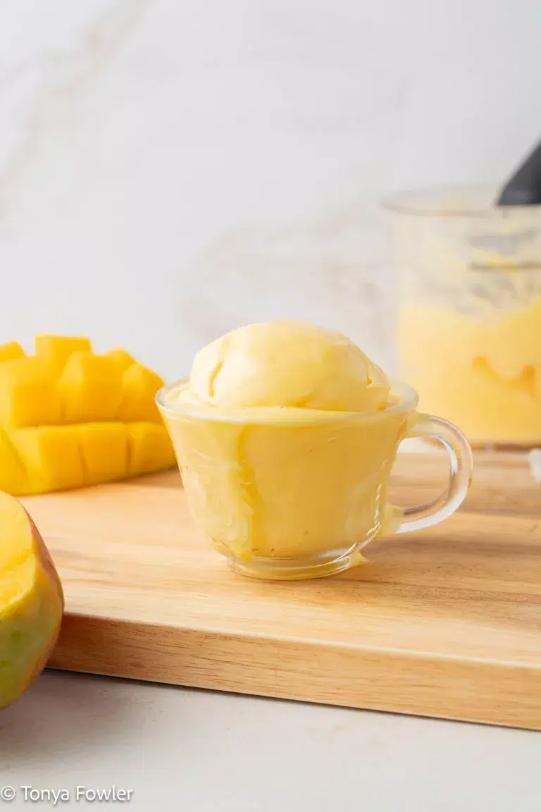 Straight on view of mango frozen yogurt in a cup with fresh mango near by.