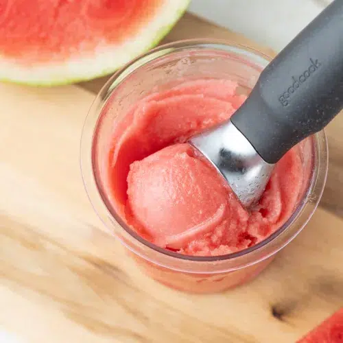 A scoop of watermelon sorbet in a container with an ice cream spoon.