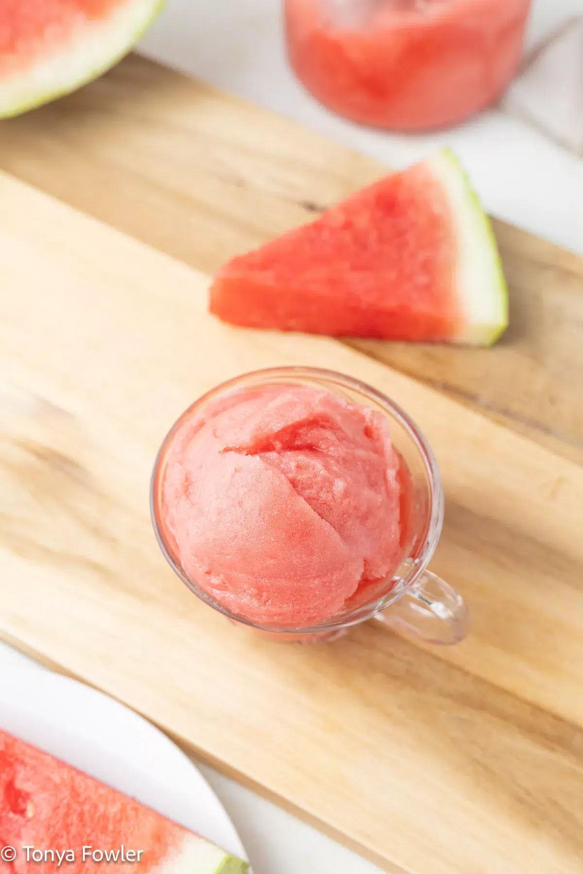 Sorbet in a cup sitting on a cutting board with slices of watermelon near by.
