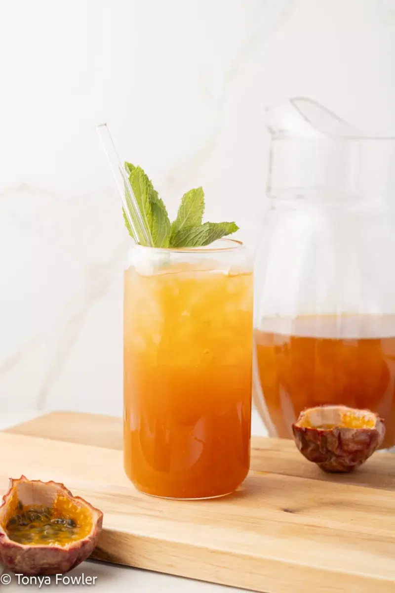 Straight on view of passion fruit iced tea in a glass with mint and fresh passionfruit.