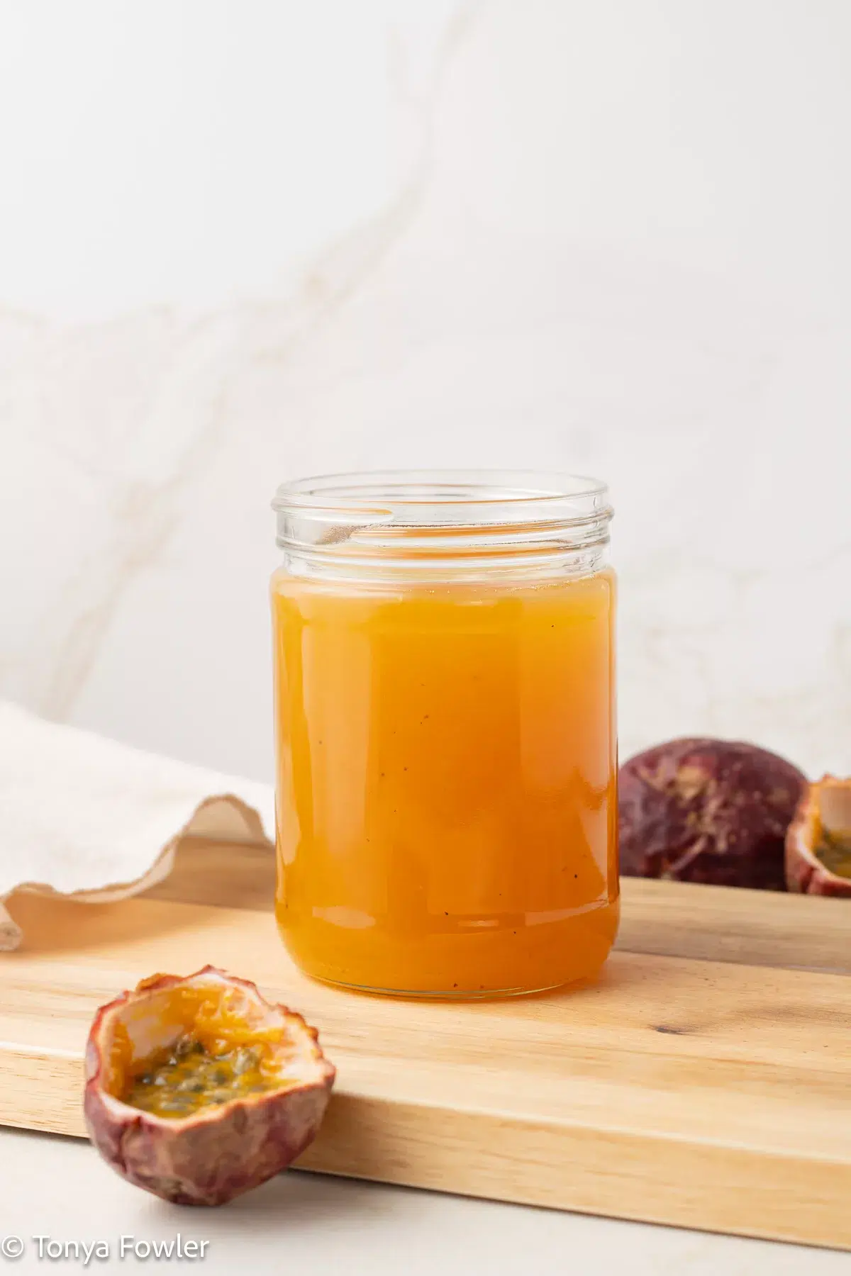 Straight on view of passionfruit syrup in a jar with fresh passionfruits.