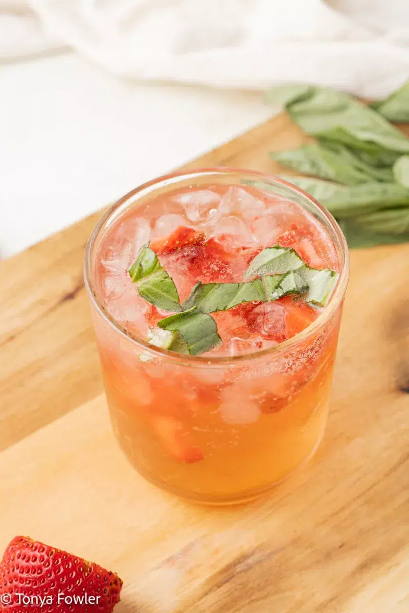 3/4 image of a strawberry basil mocktail in a glass with chopped strawberries and basil.