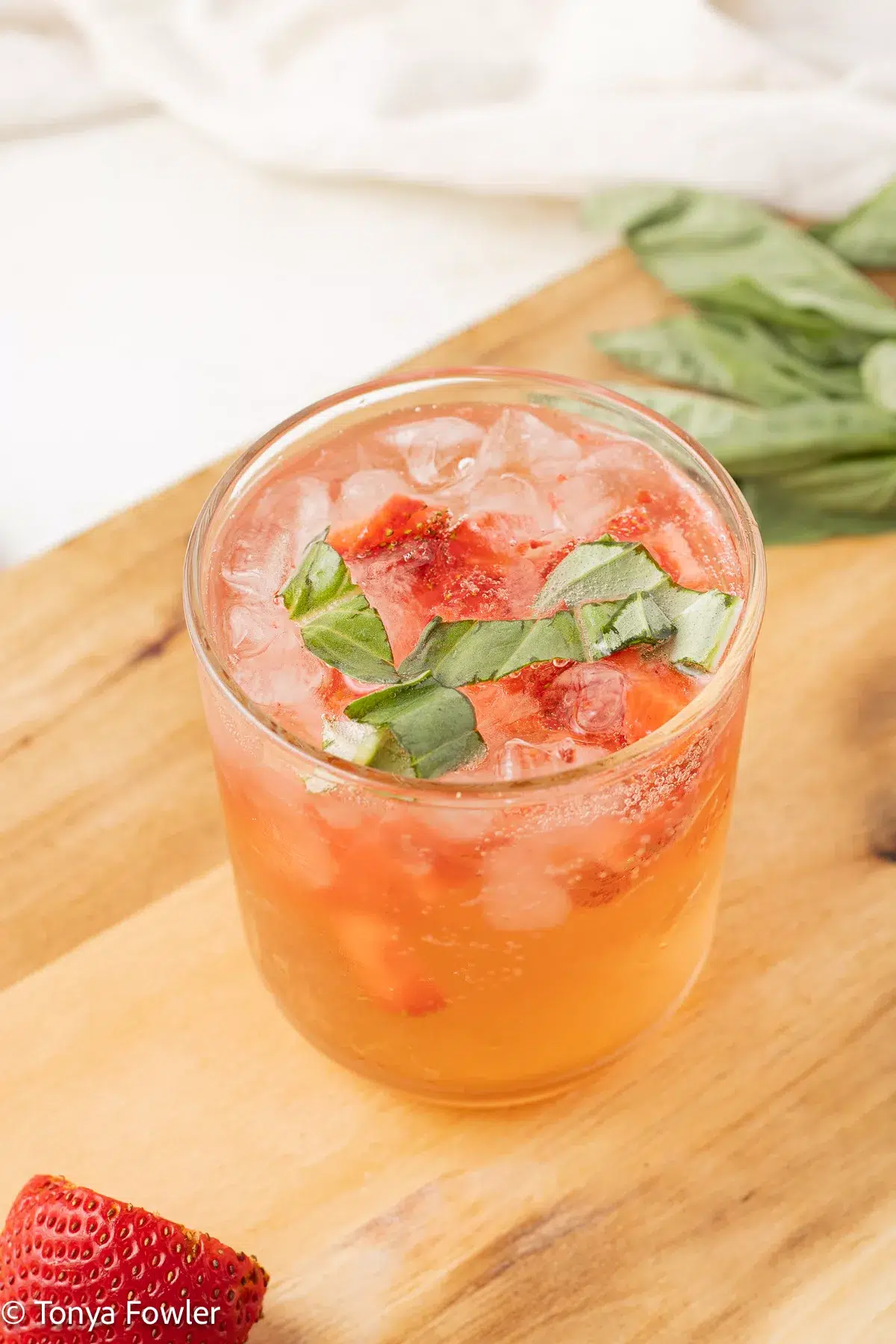 3/4 image of a strawberry basil mocktail in a glass with chopped strawberries and basil.