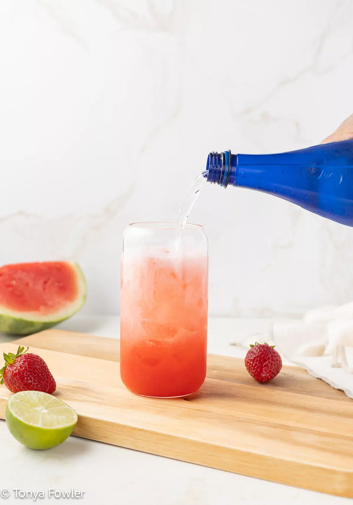 Sparkling water being poured into a glass with ice and juice.