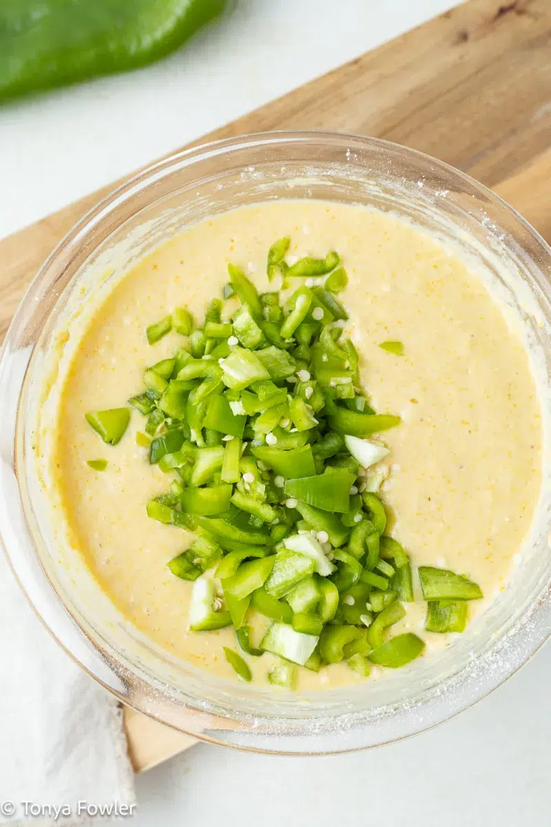 Cornbread batter in a bowl topped with chopped hatch chiles.