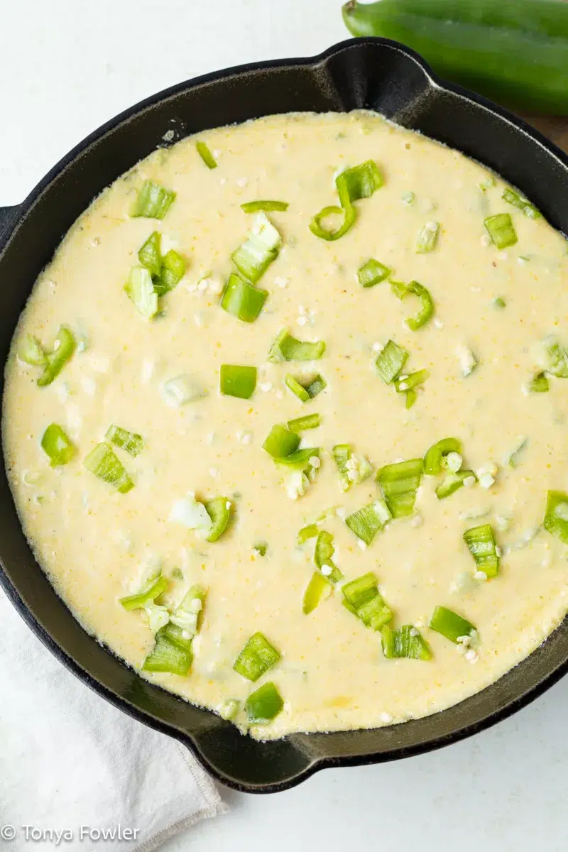 Cornbread batter in a cast iron skillet topped with chopped chiles.