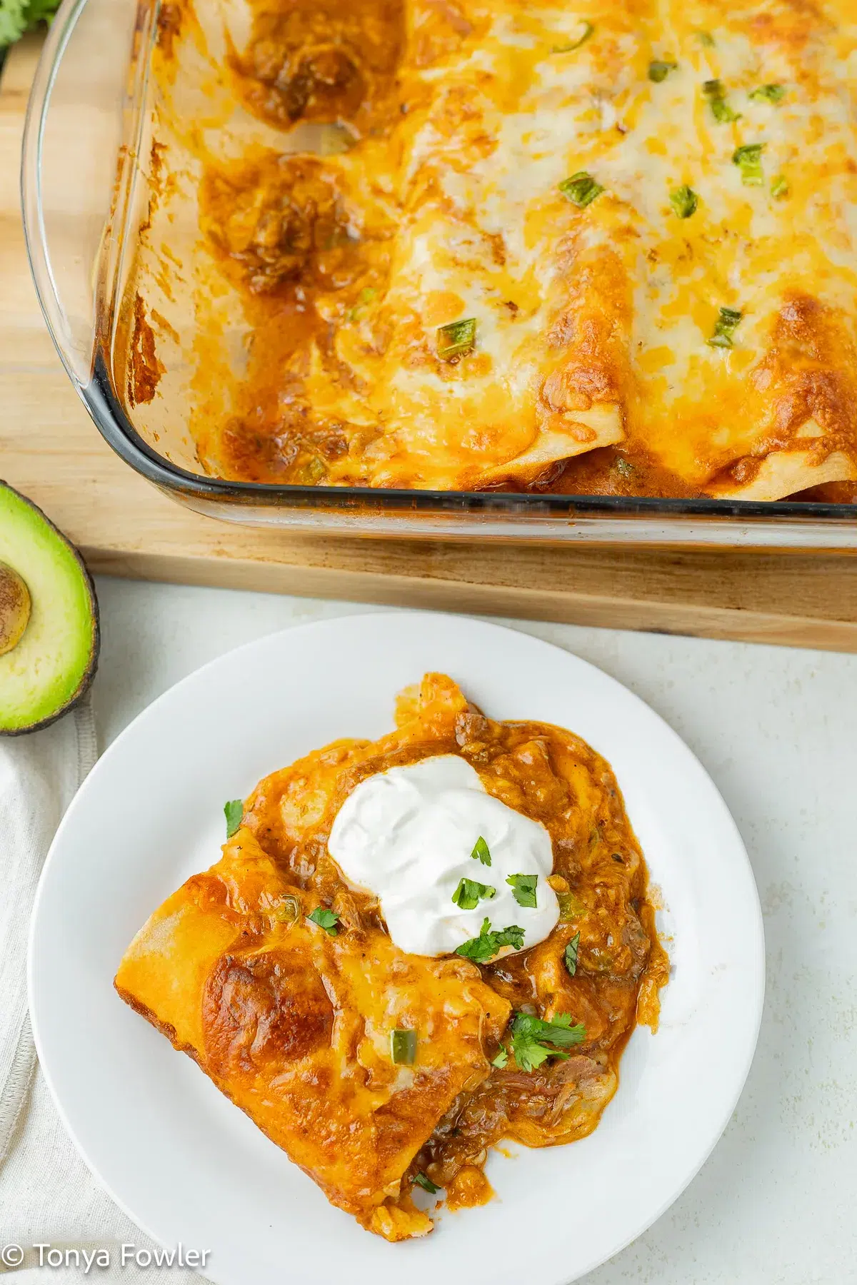 Enchiladas on a plate topped with cilantro and sour cream.