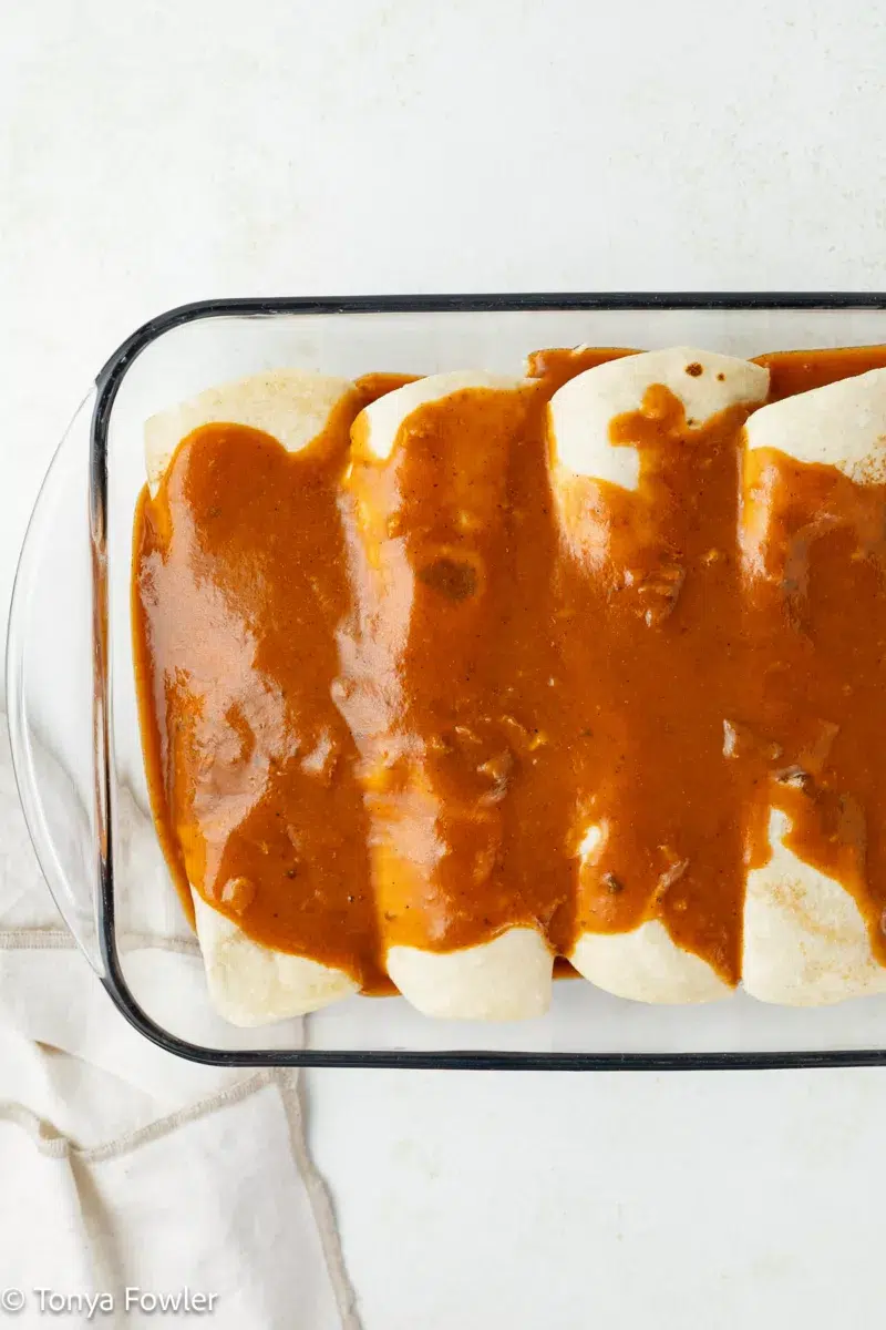 Rolled up enchiladas in a pan topped with enchilada sauce.