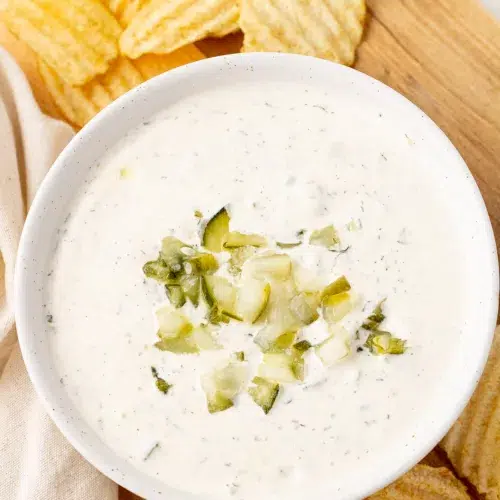 Overhead view of dill pickle ranch in a bowl topped with chopped pickles surrounded by potato chips.
