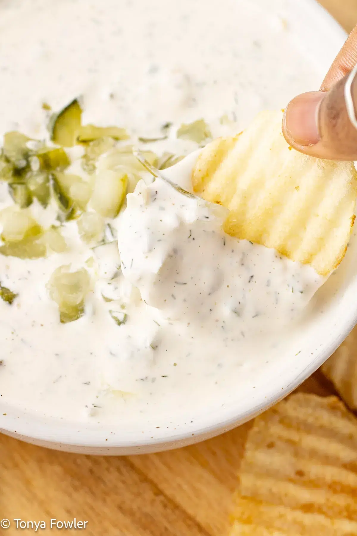 A potato chip is being dipped into a bowl of ranch.