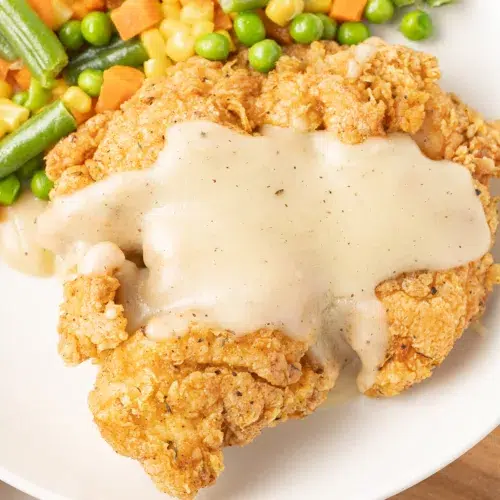 Chicken Fried Turkey Cutlets on a plate with gravy and vegetables.