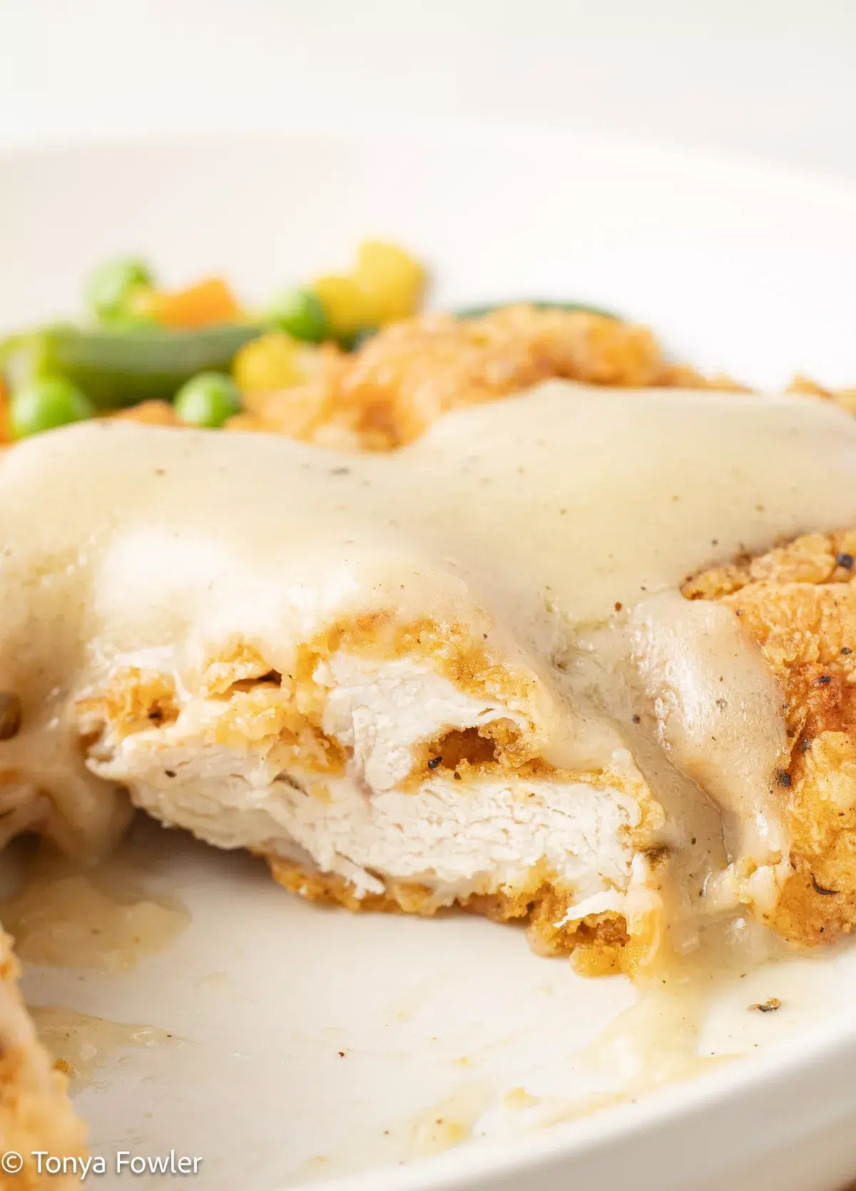 A cut slice of fried turkey on a plate topped with gravy.