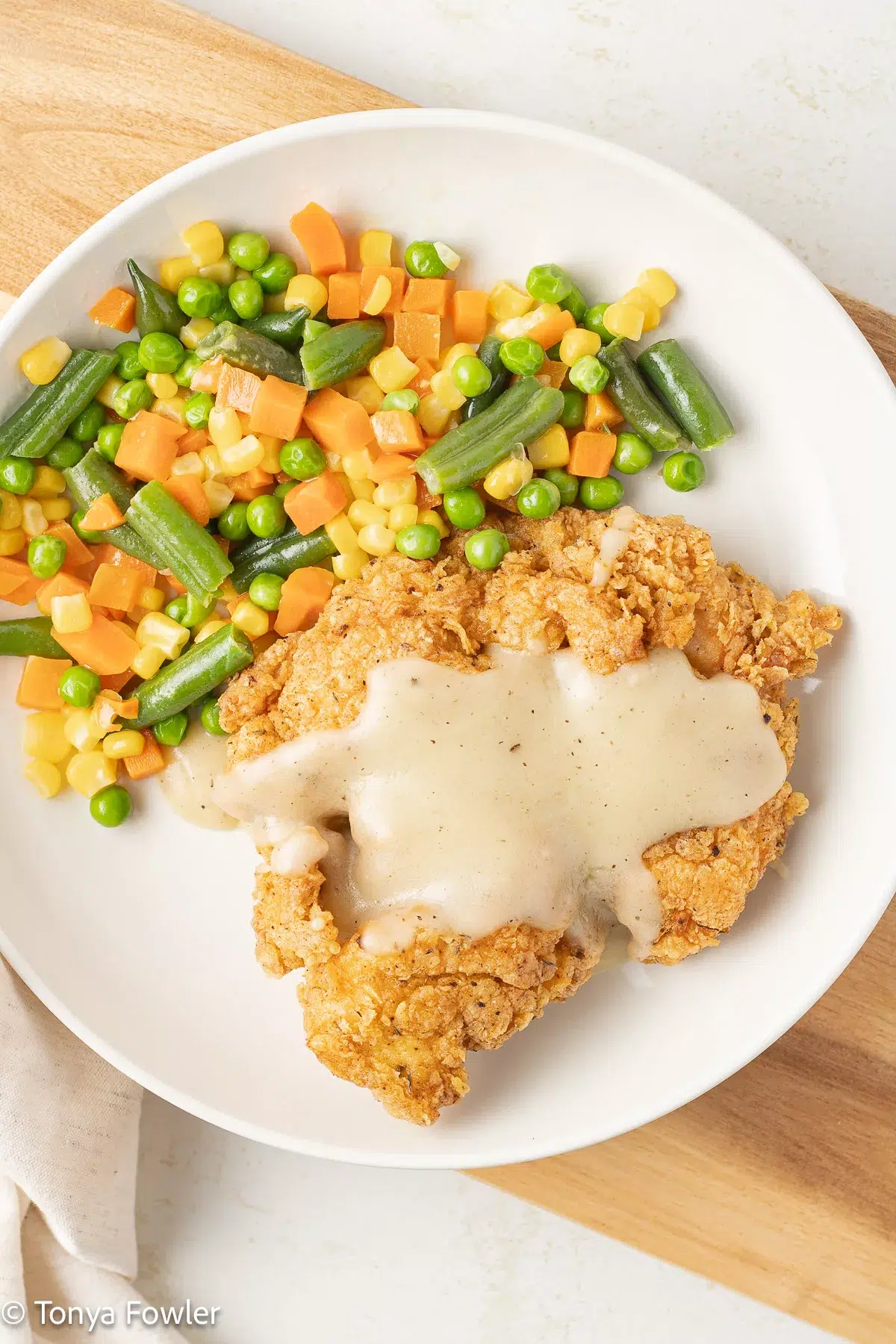 Overhead view of fried turkey on a plate with gravy and vegetables.