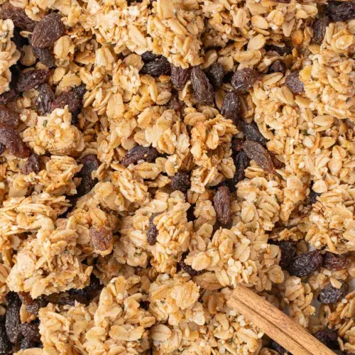 Cinnamon raisin granola on a sheet pan topped with cinnamon sticks.