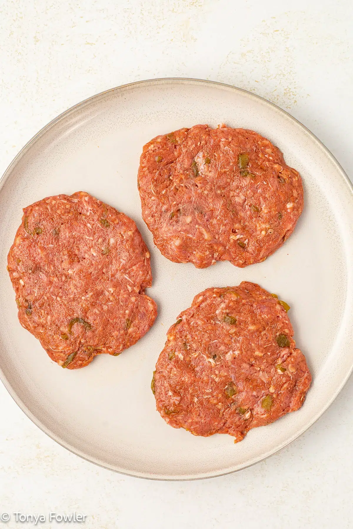 Raw meat burger patties on a plate.