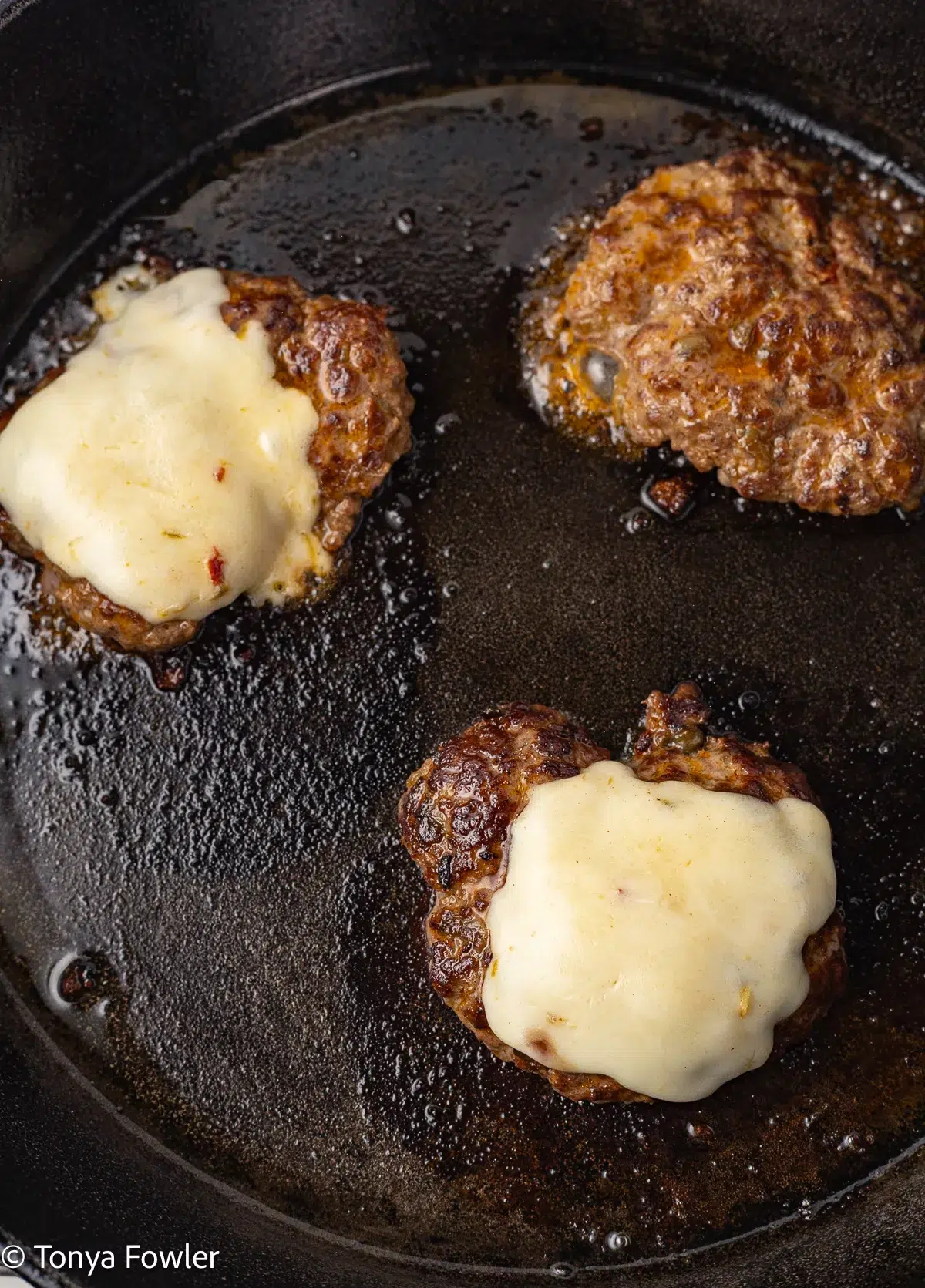 Burgers in a skillet topped with cheese.