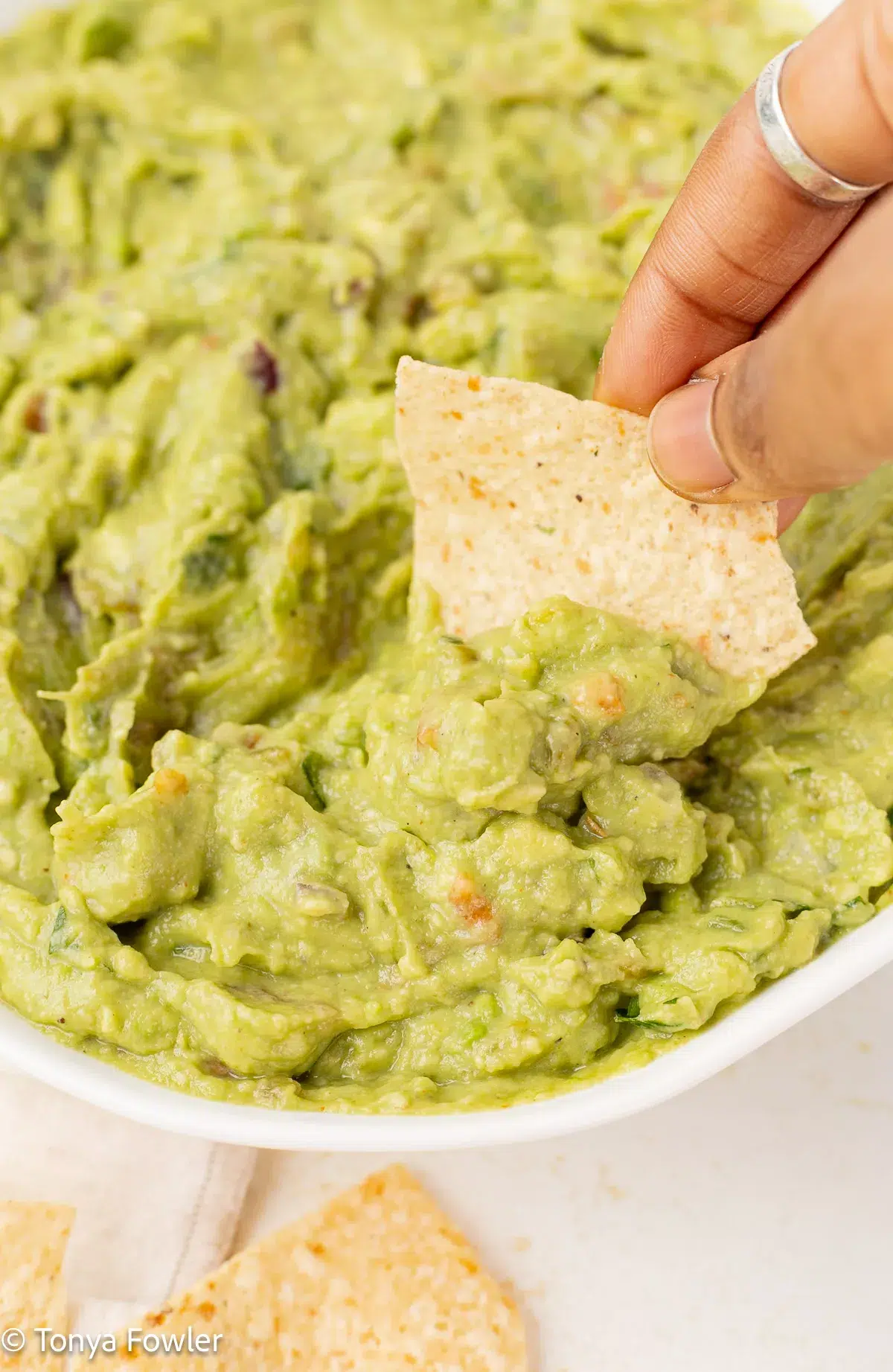 A chip being scooped into a bowl of hatch green chile guacamole.