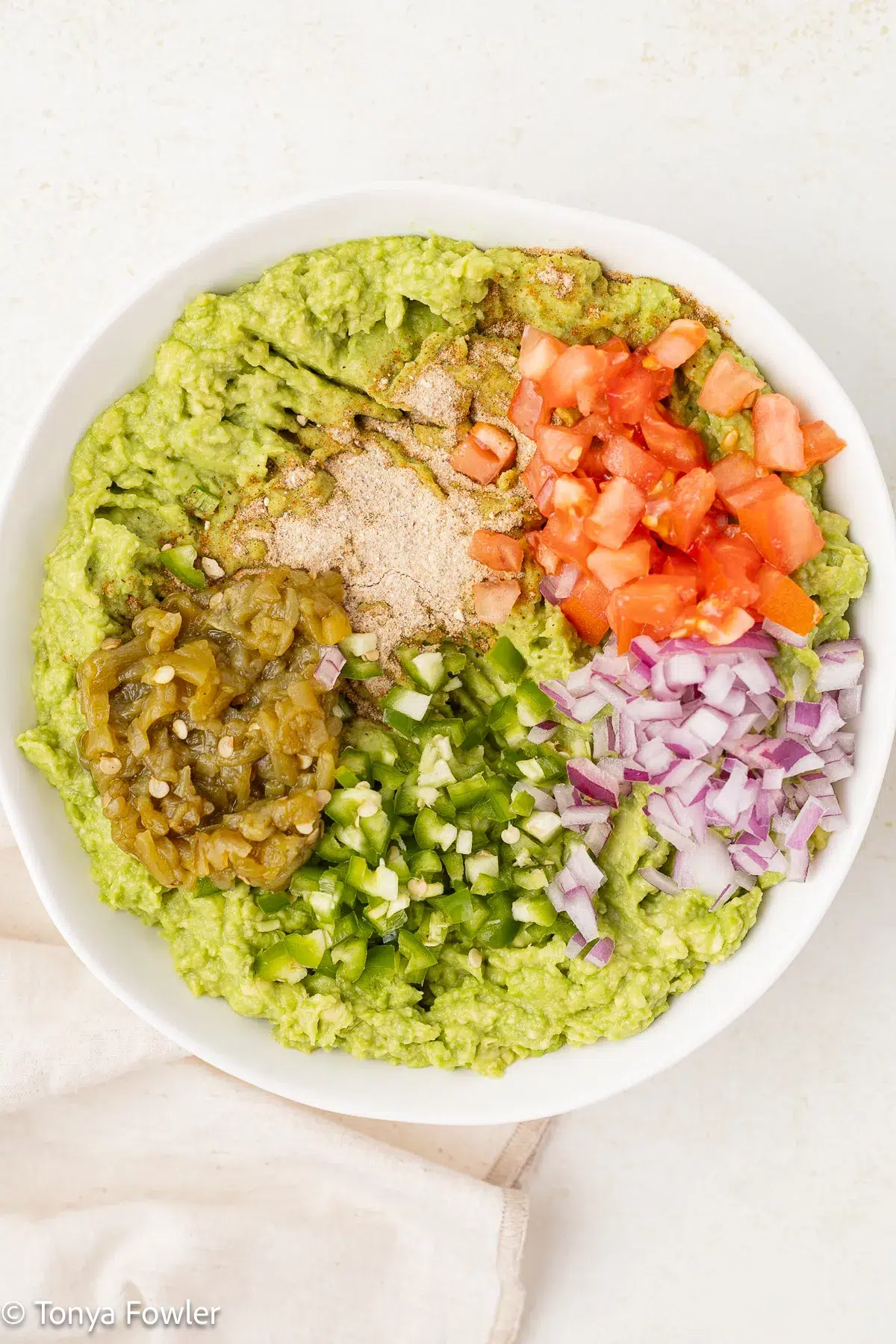 Chopped veggies in a bowl with mashed avocados.