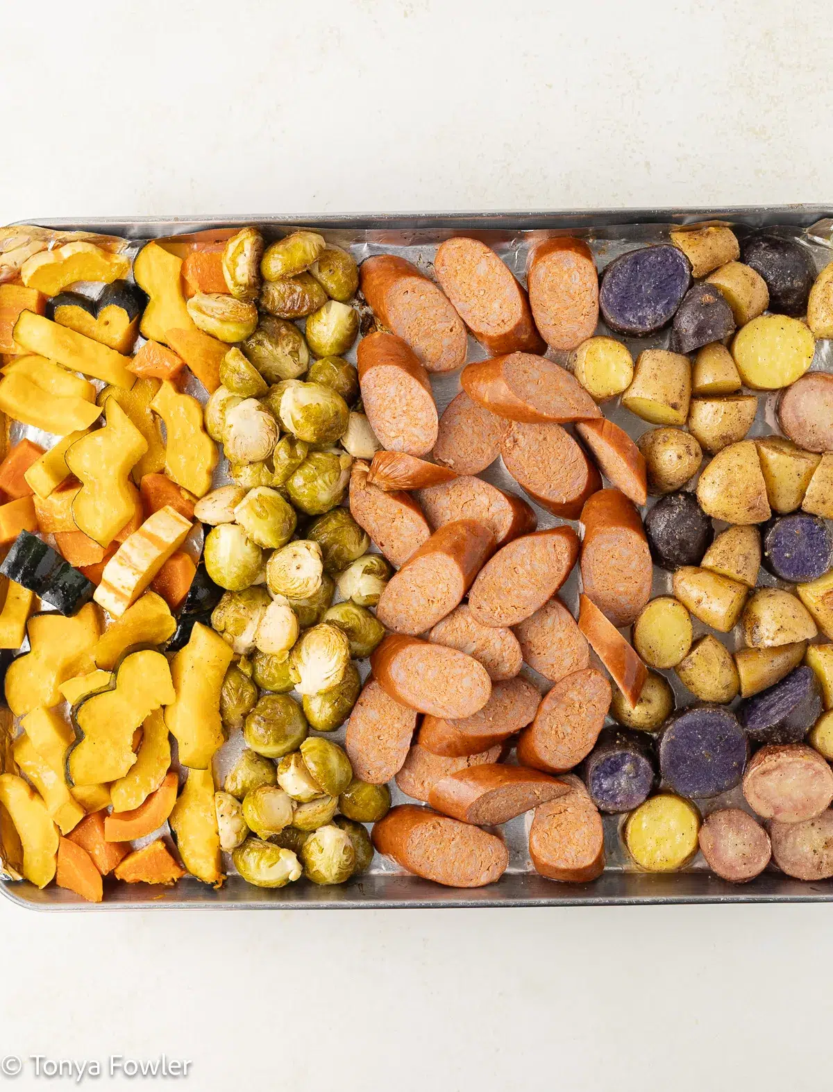 Cooked veggies on a sheet pan with uncooked sausage.