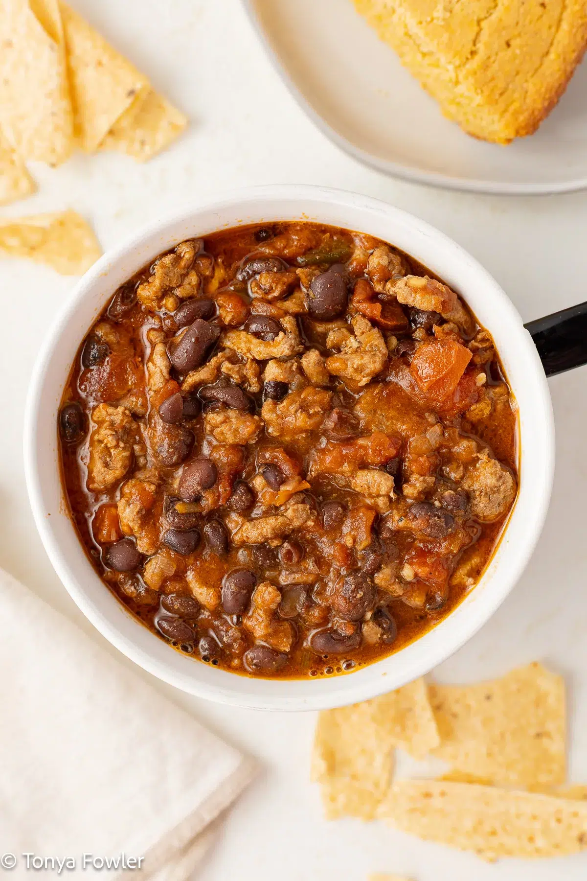 Chili in a bowl surrounded by tortilla chips and cornbread.