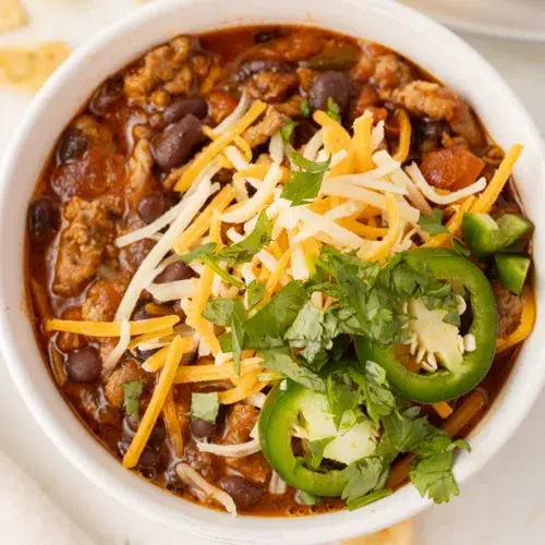 Spicy Ground Turkey Chili with Black Beans in a bowl topped with cheese and jalapenos.