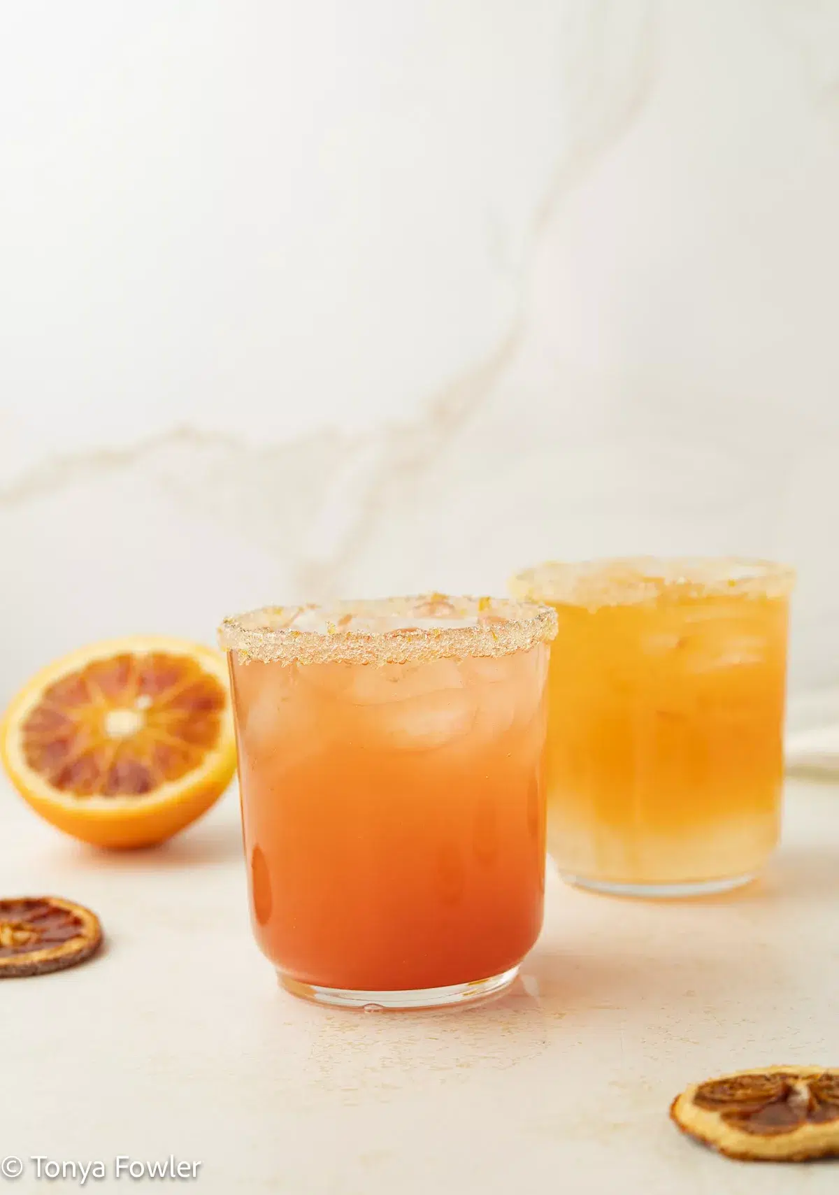 Straight on view of a couple of citrus mocktails on a counter with dried orange slices.